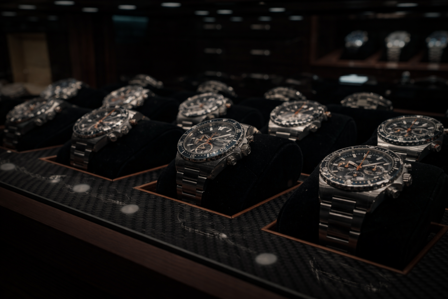 Rows of pre-owned luxury watches on black velvet cushions in a dark display case under spotlights